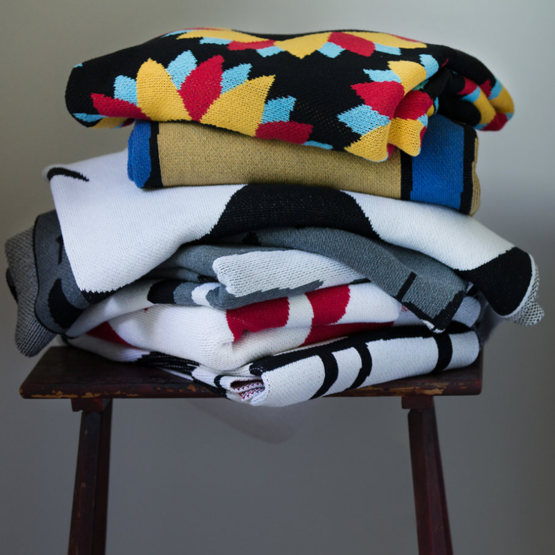Stack of woven throw blankets featuring Ryan Cronin artwork, made in USA from upcycled cotton